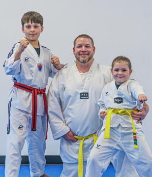 A father and two children in Taekwondo uniforms posing with their fists up