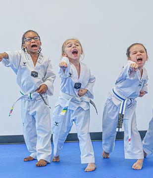 Three Little Tigers students in white uniforms punching and shouting together