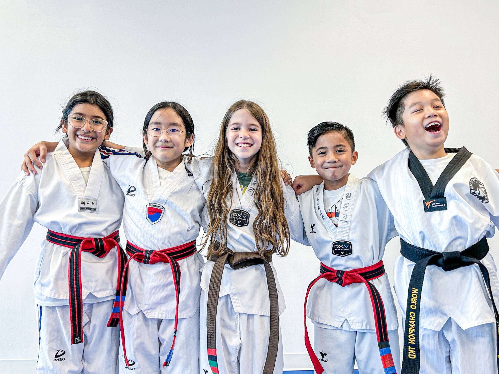 Five smiling Taekwondo students in uniform with their arms around each other
