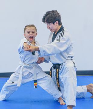 Instructor guiding a young student through a low stance on the mat